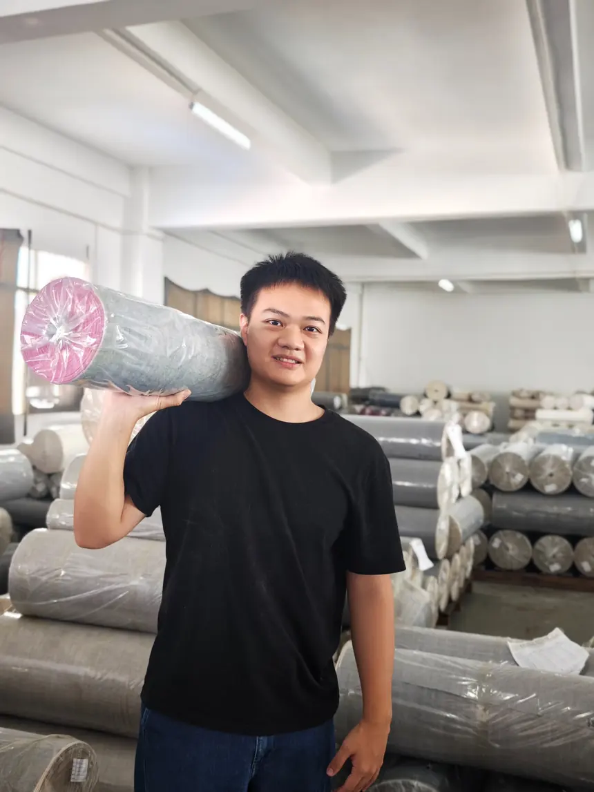 Him, HIMDENIM denim sourcing and project coordinator, holding a roll of denim fabric in a textile warehouse