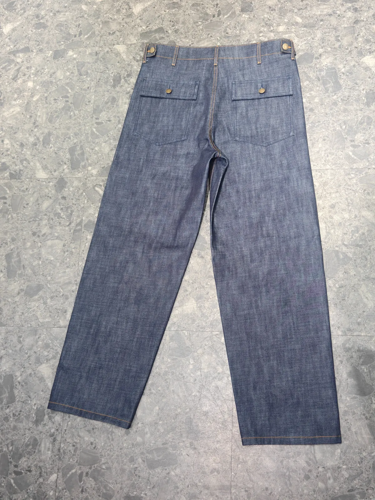Back of straight-leg indigo denim trousers with flap pockets and metal buttons