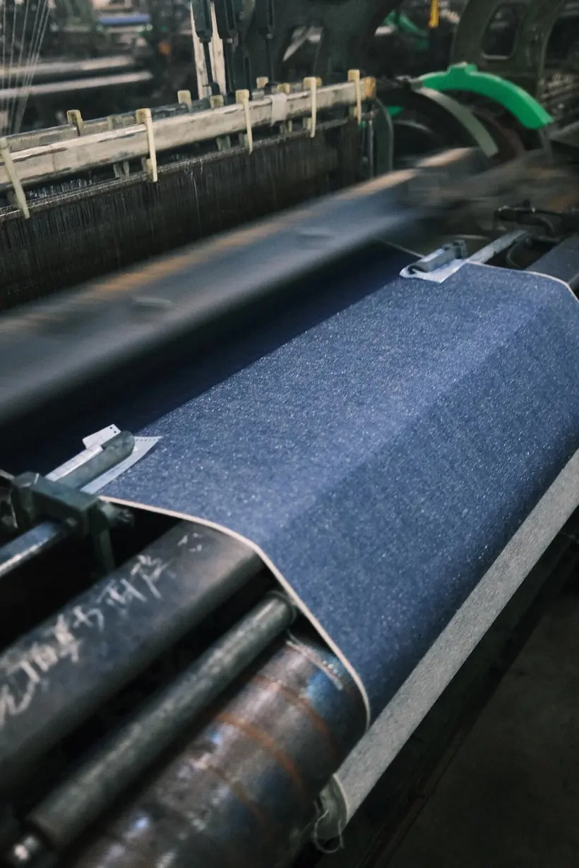 Factory Indigo selvedge denim fabric running across the rollers of a textile weaving loom
